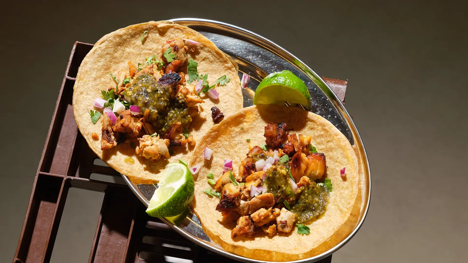 Two fresh Salsa Shop chicken tacos with salsa verde and lime on a steel plate